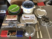 Photo showing kitchen assortment including Rival crockpot, vintage Corning dish, heart-shaped mold, double rosette timbale iron, Nordic Ware Krumkake iron in box, outdoor plastic plates and bowls, butter molds, and utensils.
