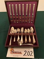 Full view of the silver plate flatware set inside the burgundy velvet-lined chest showing knives in the lid, forks, spoons, and serving pieces arranged in the bottom compartment.