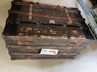 Top front angle view of large wooden storage trunk showing wear and metal accents.