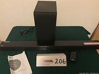 Full front view of the wireless sound bar, subwoofer, remote, and instruction manual on table.