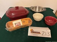 Full view of all items on green cloth: maroon covered baking dish, stainless steel bowl, two Longaberger basket weave bowls, and sealed Longaberger cracker basket with divider and insert.