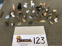 Photo showing approximately 30 small porcelain and china animal, bird, and reptile figurines arrayed on a flat surface with lot number card for reference.