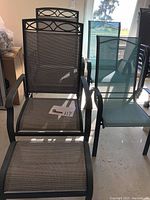 Two dark gray adjustable-back patio chairs each paired with matching ottomans in front, and a stack of teal chairs beside them, showcasing the full six-piece set.