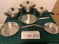 Top-down view of entire cookware set arranged on green cloth, showing all pots and pans with lids and handles.