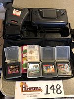 Photo showing Sega Game Gear console, Game Genie device, power adapter, four game cartridges in cases (NBA Action, Columns, Sonic 1 and Sonic 2), and carrying case.