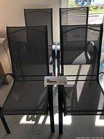 Four gray metal stackable patio chairs with dark mesh outdoor fabric seat and backrest.