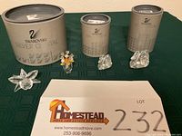 Four Swarovski Silver Crystal figurines displayed with their three original boxes on a green cloth. Includes iris flower, flower bouquet, and two swan figurines.