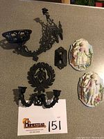 Four items arranged on a countertop: two ceramic wall plaques and two black cast iron wall sconces, showing lot composition.