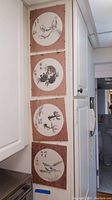 Four vertical hanging art panels mounted on a white door. Each panel has a circular central ink painting of shrimp or fish, bordered with pink floral fabric.
