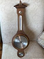 Front view showing the full wooden barometer with triangular top, thermometer in the middle, main barometer dial, and lower circular hygrometer dial.