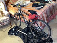 Full view of black Cannondale men's road bike leaning against a bed, with a portable bike pump lying on a black cover on the floor and various items on the bed.