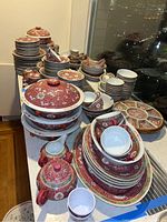 View of entire Chinese dinnerware set showing plates, bowls, spoons, lidded dishes and teapots with intricate red floral pattern on white porcelain.