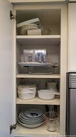 Kitchen cabinet with multiple kitchen items including nested casserole dishes, plates, and measuring cups.
