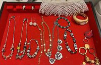 Overview of the red jewelry tray featuring multiple charm bead necklaces and bracelets, plus earrings and a white mesh bag