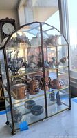 Front view of the curio cabinet showing all shelves and shell art figurines inside with natural daylight from window.