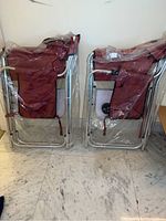 Two red folding chairs folded and wrapped in plastic, seen side by side showing metal frames and red seats.