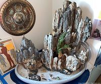 Wide angled photo showing the full ceramic fountain with lava-like stone formations and various figurines on top and around it on an oval ceramic dish base. Wall art and other decor visible in background.