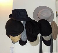 Collection of mostly black and beige men's hats hung on a wall rack