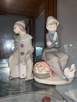 Two Lladro porcelain figurines, one male and one female, displayed together on a glass shelf.