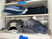Folded men's active casual wear including shirts and tops in various colors and patterns inside a white cabinet.