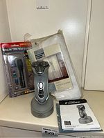 Full shot showing all the items in the lot: Norelco shaver with charging base and manual, sheer window panels in packaging, Mity Lite flashlight system, and an eye mask package.
