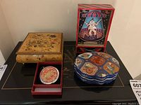 Four decorative boxes displayed together: wooden musical jewelry box, dancing clown shadow box, porcelain trinket dish, and compact mirror in box