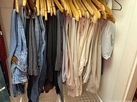Pants on wooden hangers in a closet showing a mix of light and dark colors, mostly slacks and jeans.