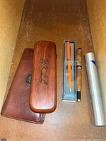 Wooden pen case, leather pen pouch, and three pens including orange, wood-grain, and metal tube case pen.