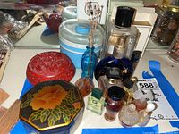 Overview of assorted perfume bottles and trinket boxes on blue cloth with mirror background.