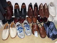 Full lot view showing 10 pairs of shoes arranged on floor and shoe rack, including dress shoes, loafers, sneakers of various brands and colors.