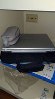 Closed silver Sony VAIO laptop with VAIO logo, black carrying case, and gray pouch on top, sitting on a surface.