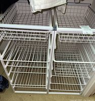 Two white metal wire storage organizers side by side, each with multiple wire basket drawers and slide-out shelves, showing open storage compartments and wire grid construction.