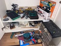 Wide view showing the organizer with multiple drawers, assorted screws, nails, tape, sandpaper, hand saw, and other tools scattered on shelves and floor.