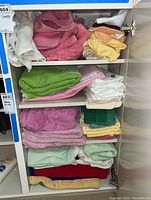 Full view of cabinet shelf with stacked and folded variety of towels in assorted colors.