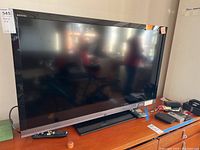 Front view of Sony Bravia TV with large black screen and silver trim on stand, no remote visible on screen.