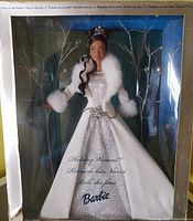 Front view of Barbie doll inside original box showing full outfit including silver dress and white faux fur cape. Box has slight damage at bottom left corner.