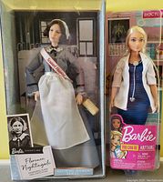 Photo shows both Barbie dolls in their original packaging side-by-side: Florence Nightingale in historical nurse uniform holding a lamp, and a modern doctor Barbie in navy dress and white coat with stethoscope.