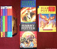 Displays the four-volume boxed set with spines visible and three additional hardcover books with illustrated covers all arranged on a red surface.