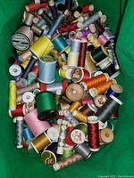 Photo showing large number of colored sewing thread spools in a green carry bag.