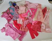 Full view of the full lot of vintage Barbie pink doll clothes laid out on a surface showing various items including dresses, pants, and tops in pink shades.