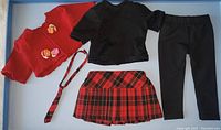 Full view of the red sweater, black shirt, black leggings, tartan skirt, and tartan necktie laid out flat on a white background.