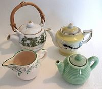 Four miniature ceramic teapot and creamer pieces displayed together on white surface.