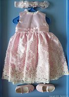 Full view of pink silk dress with lace accents on hanger with matching shoes placed below