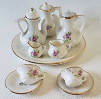 Full tea set including teapots, cups, saucers, creamers, sugar bowl on round serving plate.