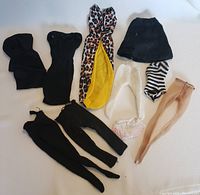 Collection of vintage Barbie clothes including black fabric pieces, leopard print dress with yellow lining, various hosiery and pantyhose.