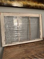 Front view of vintage 3 pane wood window shrink wrapped and placed on wooden surface.