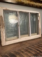 Photo of one vintage wooden window frame showing three glass panes with white paint chipping on the frame.