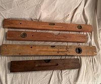 Top-down view of four vintage wooden spirit levels arranged parallel on cloth background showing different lengths, metal fittings, and weathered wood surfaces.