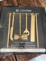 Photo of the full boxed set, showing the five gold plated bar tools on a white marble base inside clear packaging.
