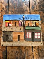 Front view of the coastal village art piece on a wooden table, showing colorful textured houses with mixed materials and a central utility pole.